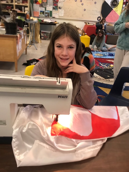A child sitting at a table with a sewing machine

Description automatically generated